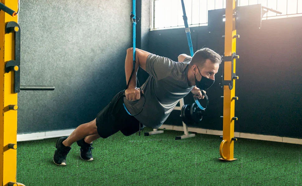 Man wearing face mask doing TRX suspension push-up exercise in gym with artificial turf