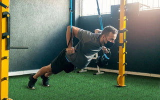 Man wearing face mask doing TRX suspension push-up exercise in gym with artificial turf