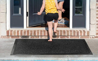 Child walking barefoot on black non-slip rubber door mat outside brick home entrance