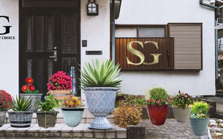Front porch with black door, decorative potted plants, pink flowers, and SG logo on white wall